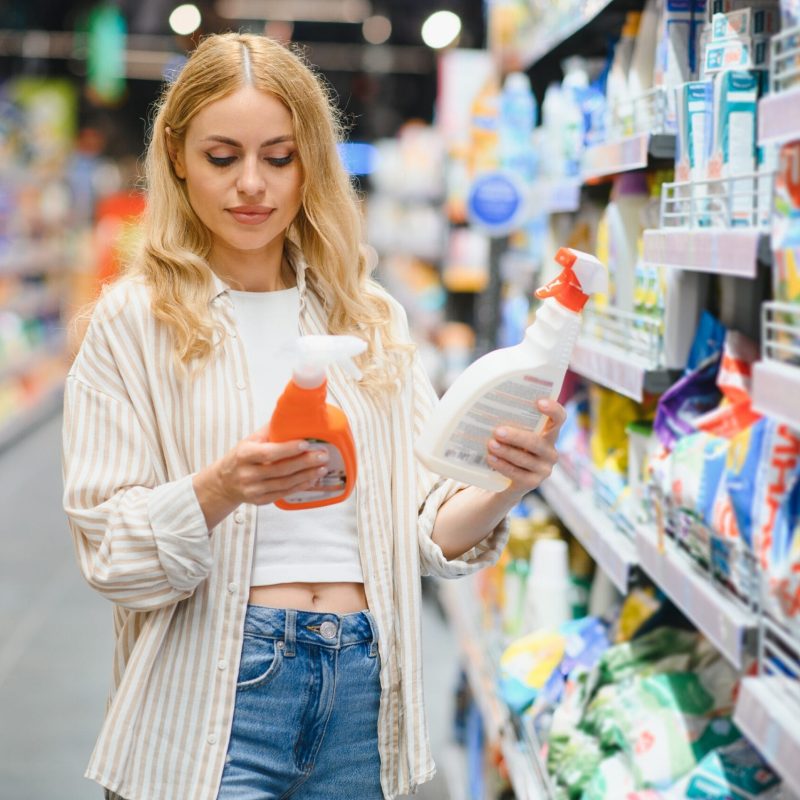 Young glad smiling woman buying household chemicals or laundry detergent at supermarket.